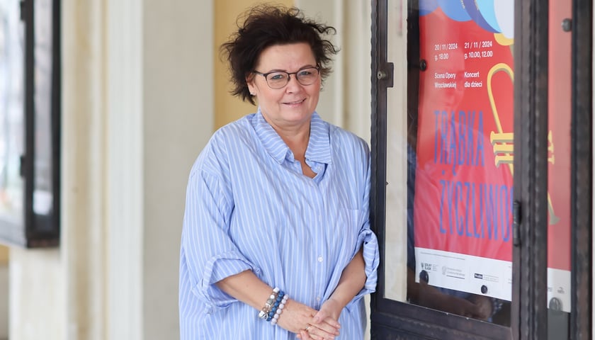 Dorota Sosna, pomysłodawczyni koncertu "Trąbka życzliwości" przy plakacie zapowiadającym go w Operze Wrocławskiej