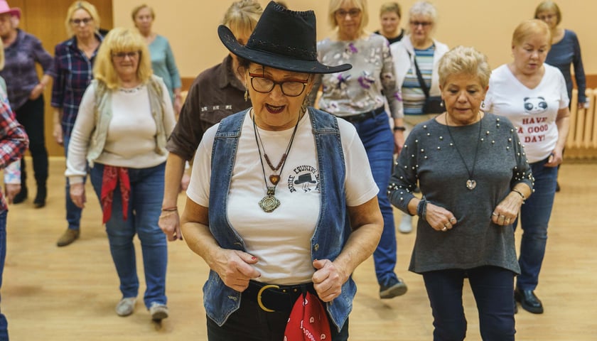 Maria Dowbecka, kierowniczka grupy tanecznej Dance Senior Country na pierwszym planie, z tyłu za tańczący seniorzy