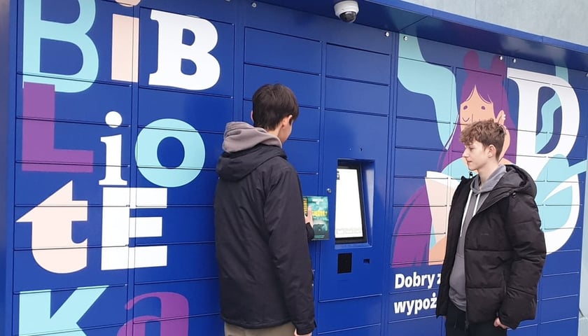 Книжкомат, який працюватиме від суботи у філії № 22 Міської публічної бібліотеки ім. Тадеуша Ружевича на вул. Chociebuska у Вроцлаві. На фото перед книжкоматом стоять двоє молодих людей