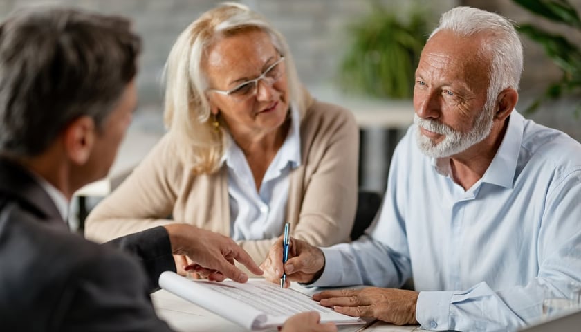 Na zdjęciu para seniorów rozmawia przy biurku z mężczyzną w garniturze