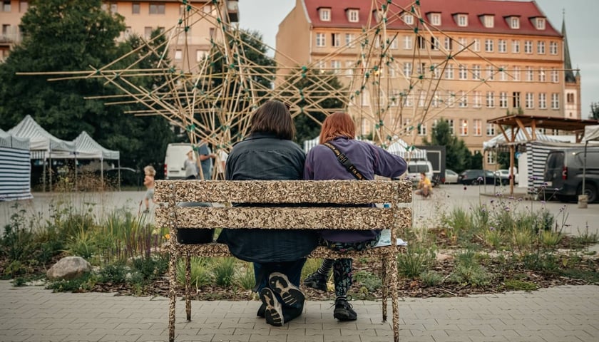 Na zdjęciu dwoje ludzi siedzących na ławeczce na Targowisku Jemiołowa