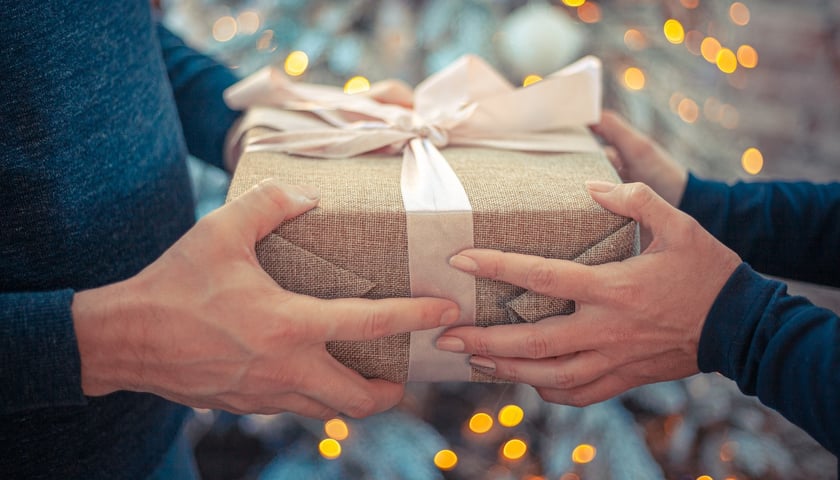 Na zdjęciu dwie osoby przekazujące sobie prezent, za nimi choinka. Zobacz, co możesz kupić na mikołajki we Wrocławiu!