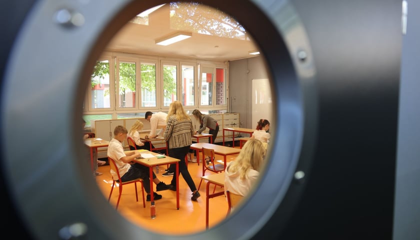 Egzamin ósmoklasisty w SP nr 29 we Wrocławiu. Przez drzwi z oddali widać uczniów siedzących w ławkach. Zdjęcie archiwalne