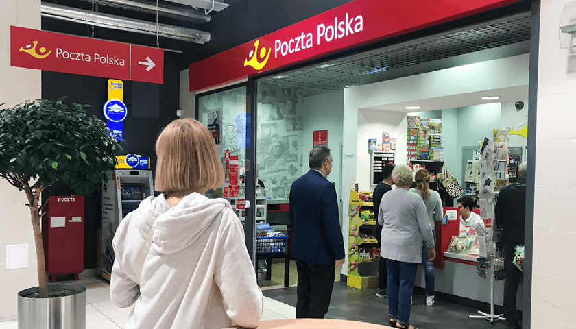 Kobiety i mężczyźni w kolejce na Poczcie Polskiej 