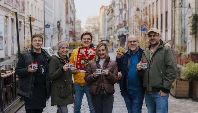7 grudnia na ul. św. Antoniego we Wrocławiu rozpocznie się Festiwal Grzańca, który będzie trwał do 22 grudnia. Na zdjęciu sześcioro organizatorów ze świątecznymi kubeczkami i plakatem.