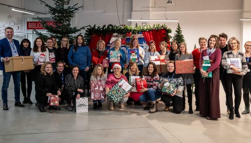 Przy choince grupa osób trzymająca paczki dla powodzian z Dolnego Śląska. Zaangażowali się pracownicy Wrocławskich Mieszkań