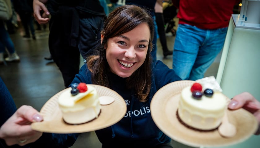 9. urodziny Hydropolis. Wrocław, 07.12.2024. Na zdjęciu uśmiechnięta kobieta w bluzie z napisem Hydropolis, trzymająca w rękach dwie babeczki na papierowych talerzykach