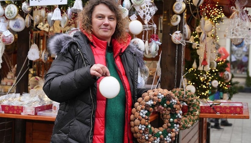Kobieta trzymająca stroik z orzechów, stoi przed drewnianą budką na Wrocławskim Jarmarku Bożonarodzeniowym