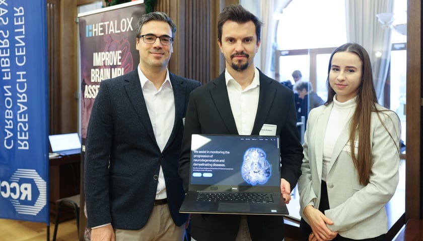 6. Polsko-Saksoński Dzień Innowacji na PWr we Wrocławiu. Na zdjęciu kobieta i dwoje mężczyzn trzymają laptopa skierowanego w stronę obiektywu