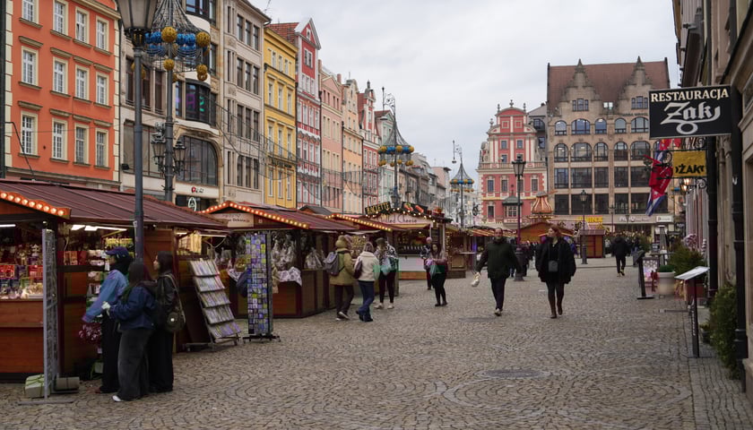 Kilka osób przechadza się po Jarmarku Bożonarodzeniowym na wrocławskim rynku.