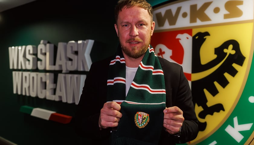 Dyrektor sportowy Rafał Grodzicki w szaliku klubowym, na tle klubowego herbu Śląska Wrocław