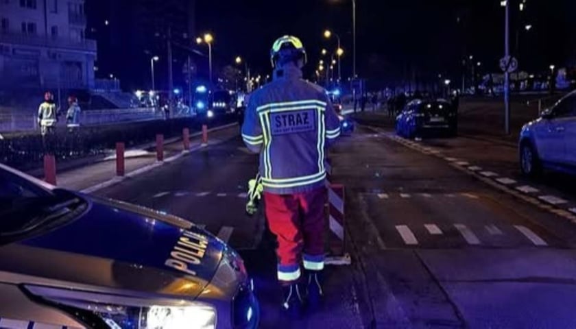 Strażak na przed budynkiem, w którym wybuchł pożar. Na pierwszym planie radiowóz policyjny 