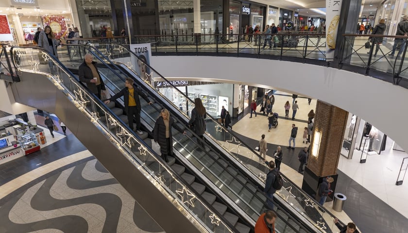 Wnętrze galerii handlowej. Na zdjęciu widać ludzi, którzy przyszli do sklepu na zakupy (jadą ruchomymi schodami)