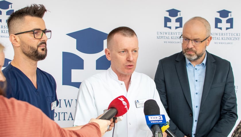 Na zdjeciu trzech mężczyzn przed mikrofonami różnych stacji radiowych i telewizyjnych. Od lewej: Andrzej Mędrala, ratownik i pielęgniarz koordynujący w SOR USK we Wrocławiu, dr Janusz Sokołowski, kierownik Szpitalnego Oddziału Ratunkowego USK, lek. Maciej Kamiński, wicedyrektor ds. medycznych USK we Wrocławiu