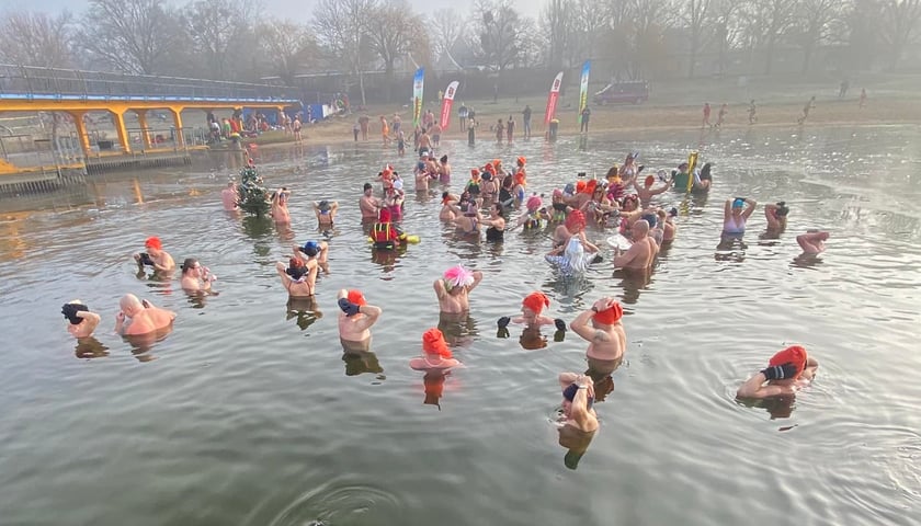 Wrocławskie Morsy na kąpielisku Morskie Oko we Wrocławiu. Na zdjęciu widać osoby, które w czapkach i kolorowych strojach stoją zanurzone w wodzie