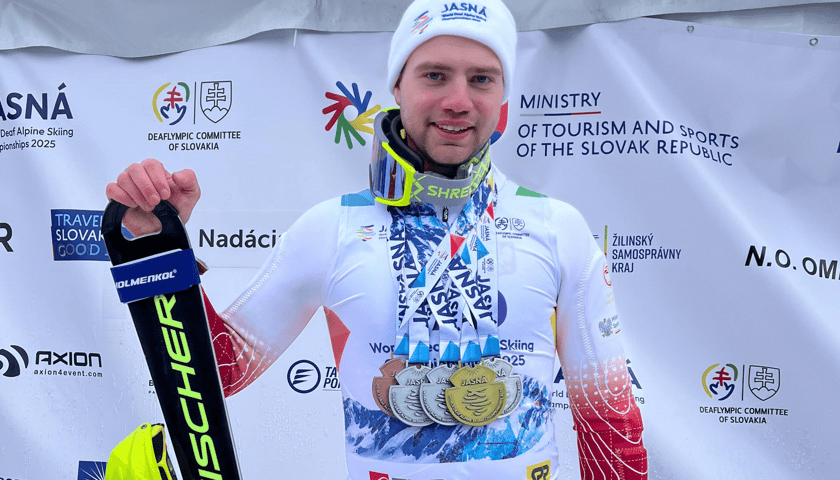 Bruno Łukaszyk, w stroju sportowym, na szyi wiszą mu medale, które zdobył. Prawą ręką trzyma narty 