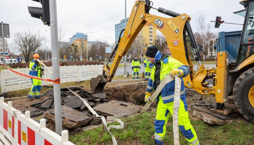 Pracownicy MPWiK w odblaskowych kombinezonach pracują przy wykopie, w tle ulica i bloki - zdjęcie ilustracyjne
