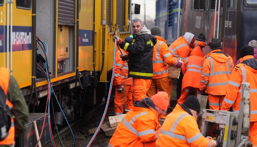 Pracownicy kolei ubrani w odblaskowe pomarańczowe stroje, którzy pracują przy pociągu, który wykoleił się na Sołtysowicach.