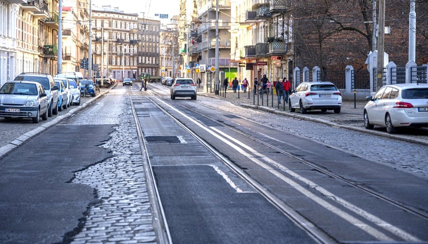 Ulica, kostka brukowa łatana asfaltem, torowisko, w tle samochody. Wrocławskie Inwestycje wybrały projektanta przebudowy ulicy Słowiańskiej i św. Wincentego na Nadodrzu
