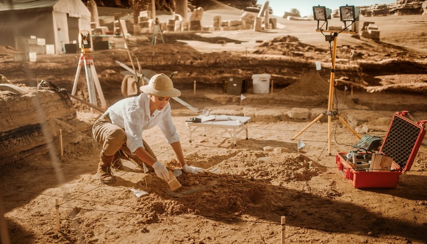 Na zdjęciu kobieta w kapeluszu pracuje na na stanowisku archeologicznym na pustyni. Zdjęcie ilustracyjne