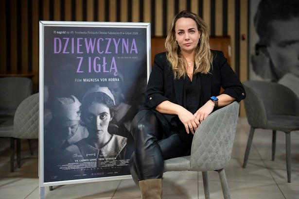 Scenografka Jagna Dobesz siedząca przy plakacie zapowiadającym film "Dziewczyna z  igłą"