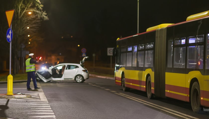 Rozbite białe Renault blokujące pas jezdni, na pasie obok miejski autobus. Miejsce wypadku z 02.02.2025