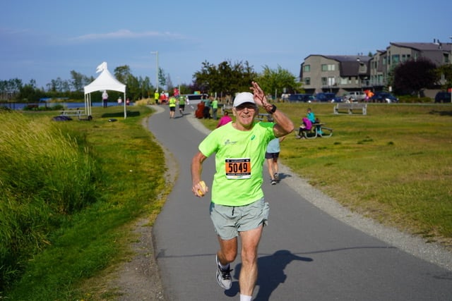Maratończyk, senior prof. Jan Chmura biegnący ostatnie 20 km w maratonie na Alasce. W tle widać innych zawodników, kibiców i domy