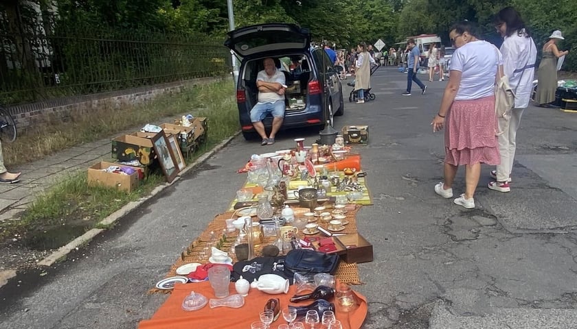 Pchli targ na Kasztanowej. Na zdjęciu widać przedmioty rozłożone na matach na ulicy oraz przechodzących ludzi