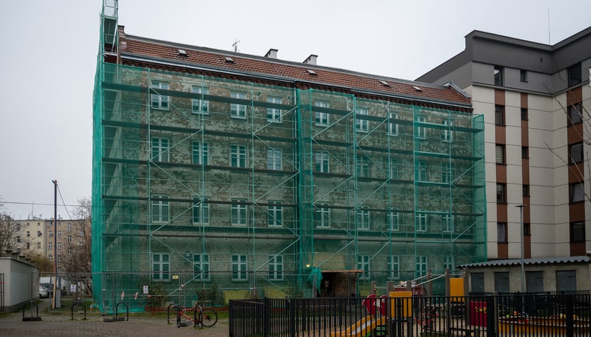 Budynek, wokół którego stoi rusztowanie z zieloną siatką