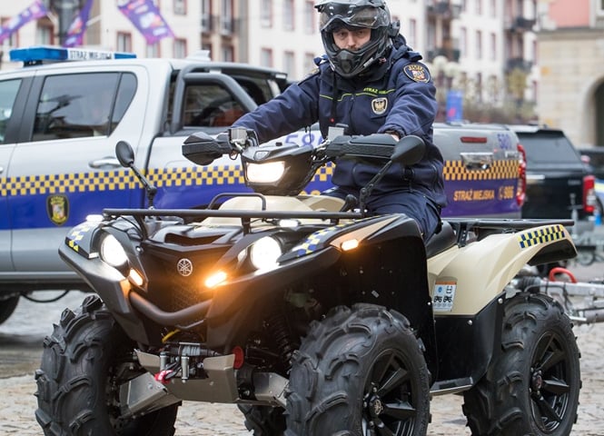 Wrocławski strażnik miejski podczas patrolu na quadzie, w tle samochód Straży Miejskiej Wrocławia