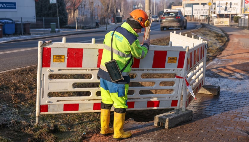 Awaria na Strachocińskiej dobiegła końca, na zdjęciu mężczyzna ustawia barierki odgradzające miejsce awarii