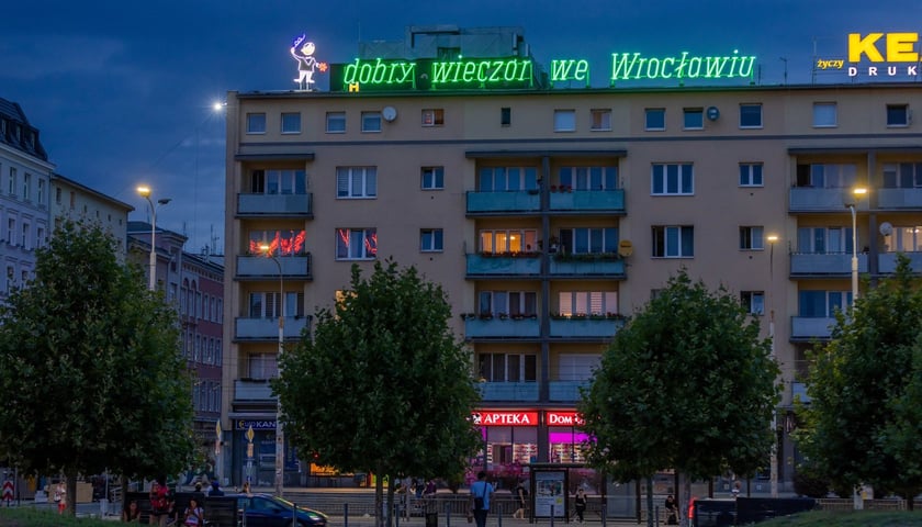 Neon "Dobry wieczór we Wrocławiu" przy ul. Pisudskiego. Na zdjęciu widać blok mieszkalny, na którego dachu jest lśniący neon