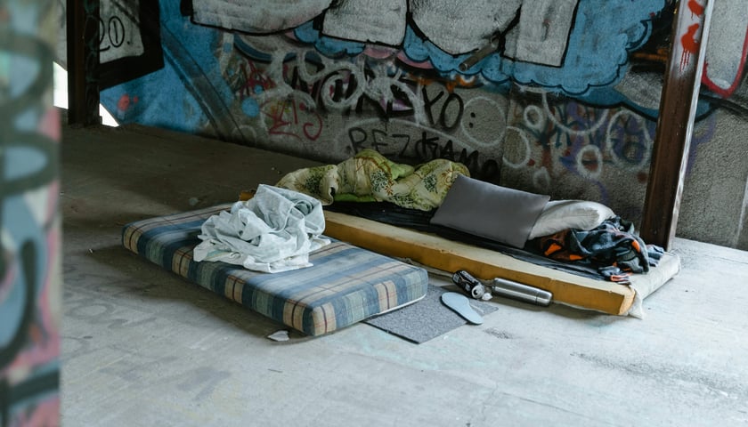 Brudne materace, na których leżą koce, w przejściu podziemnym