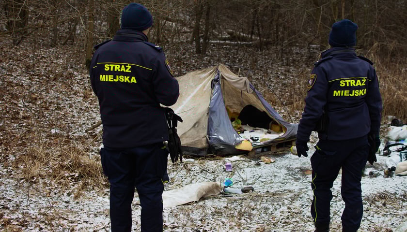 Straż miejsca na patrolu - dwoje strażników patrzy na namiot, w którym na śniegu przebywa osoba w kryzysie bezdomności