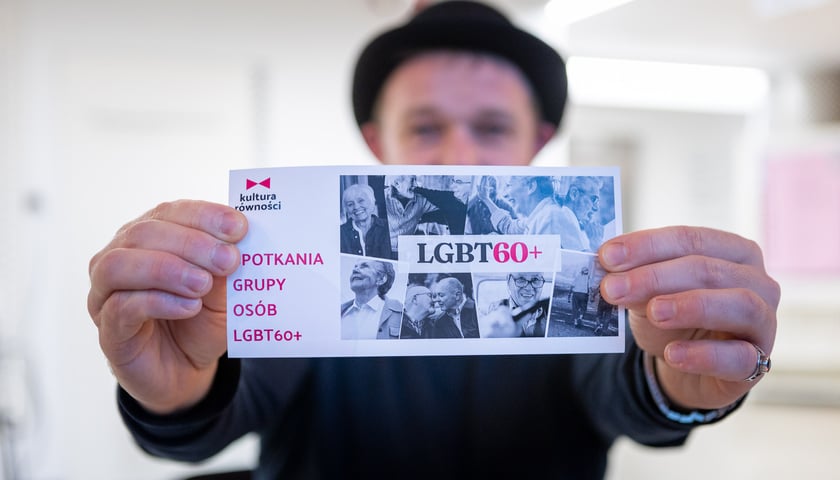 Grzegorz Grzeszczyk trzymający w dłoniach ulotkę z informacją o spotkaniach grupy LGBT60+