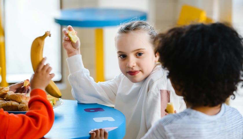 Dziewczynka i inne dzieci podczas posiłku przy niebieskim stoliku