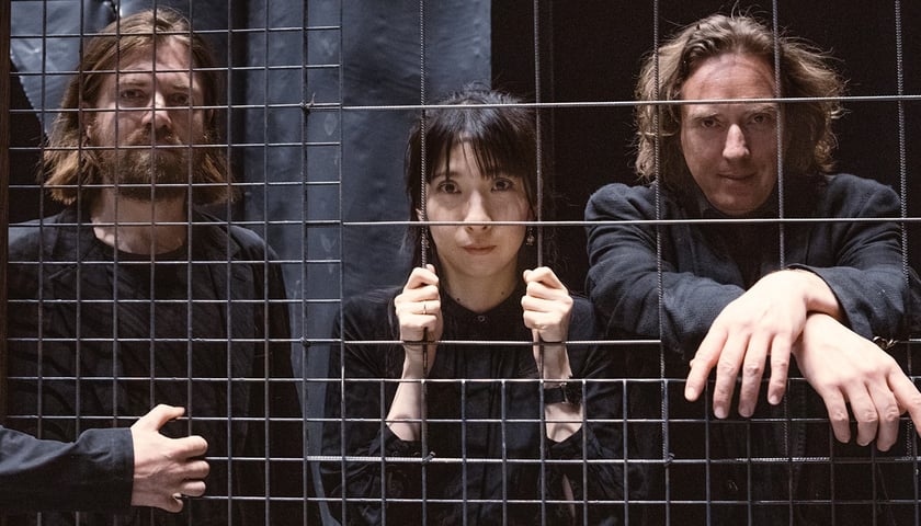 Kobieta i dwóch mężczyzn stoją za kratą, zespół Tangerine Dream