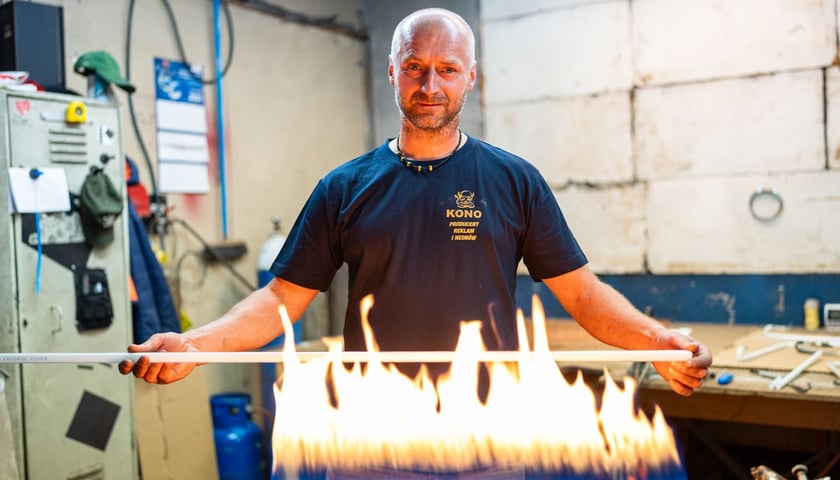 Robert Konopka trzyma szklaną rurę neonową w płomieniu