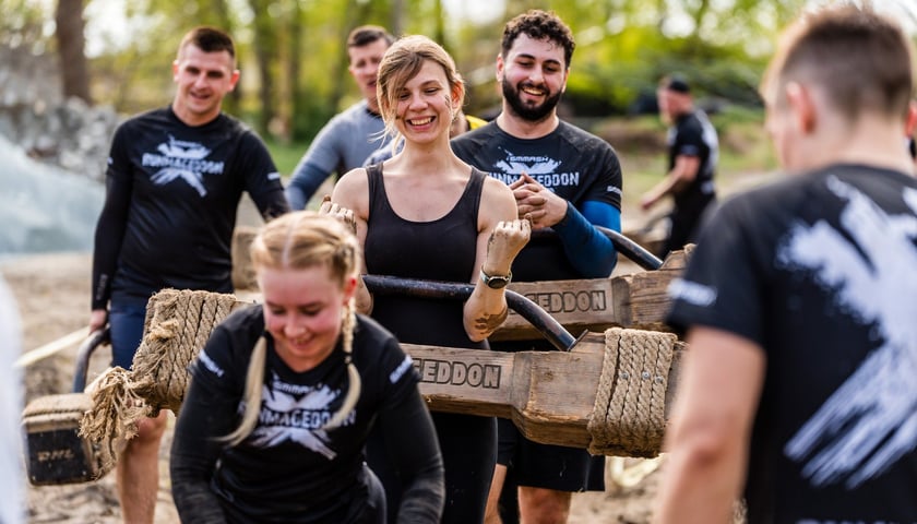 Uczestnicy Runmageddonu biegnący i niosący drewniane belki