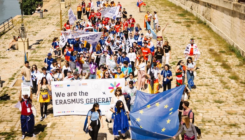 Kolorowy pochód młodzieży akademickiej z transparentem z napisem "We are the Erasmus Generation" i flagą Unii Europejskiej
