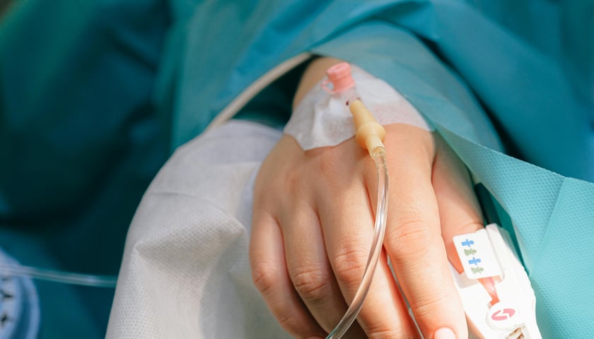 Dłoń z wenflonem przykryta niebieskim materiałem