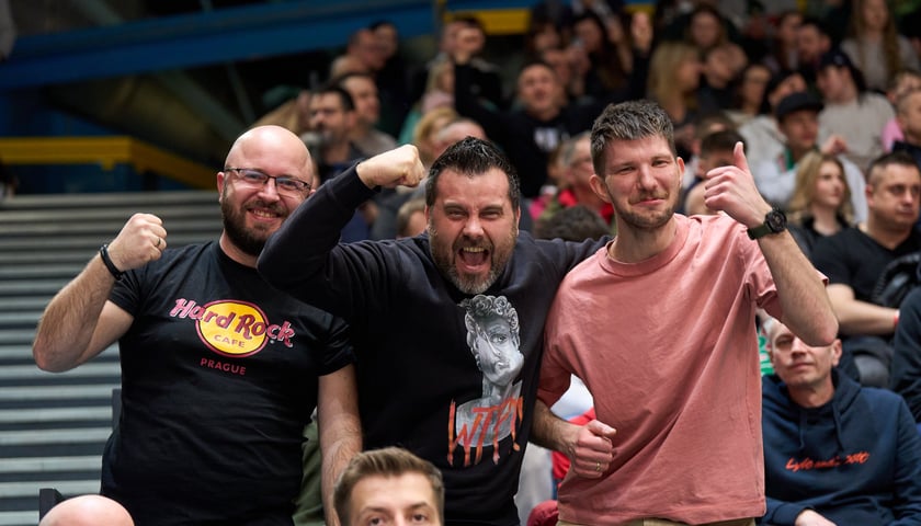 Trzech mężczyzn z uśmiechami na twarzach dopinguje swoją drużynę