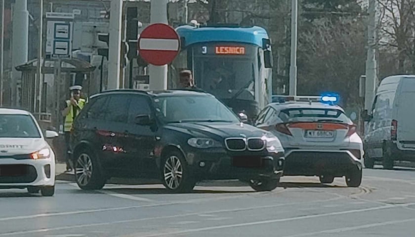 Samochód marki BMW stoi na torach, za nim tramwaj