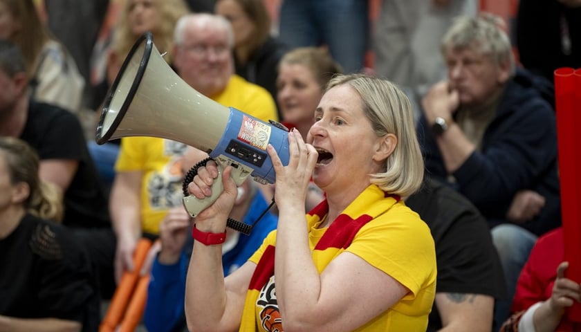 Kobieta w żółtej koszulce i z megafonem na trybunie w hali Ślęza Arena podczas 5. meczu z Gorzowem