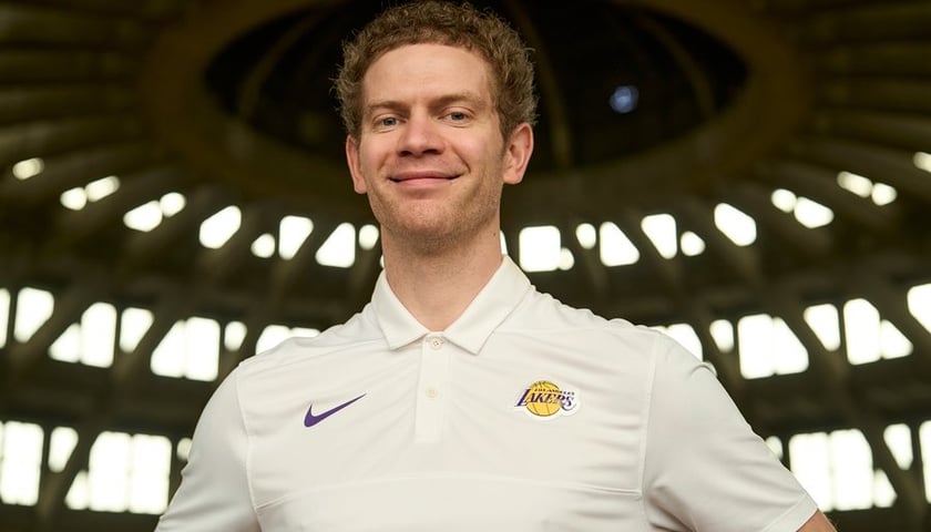 Uśmiechnięty Bronek w białej koszulce z logo Lakersów, na tle kopuły Hali Stulecia