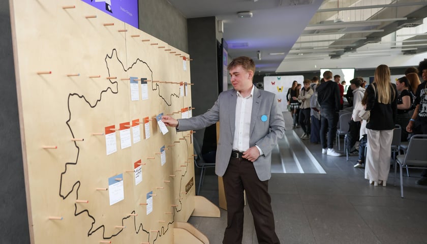 Młodzież podczas konsultacji Strategii Wrocławia 2050 - młody chłopak w szarej marynarce przyczepia karteczkę do ściany