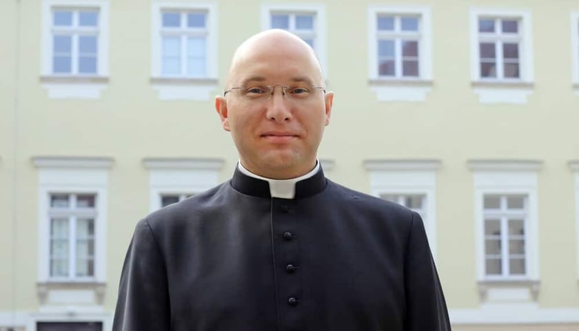 Ksiądz Mariusz Szypa, dyrektor wydziału katechetycznego kurii wrocławskiej, proboszczem parafii w Czernicy, stoi w sutannie na tle budynku na Ostrowie Tumskim