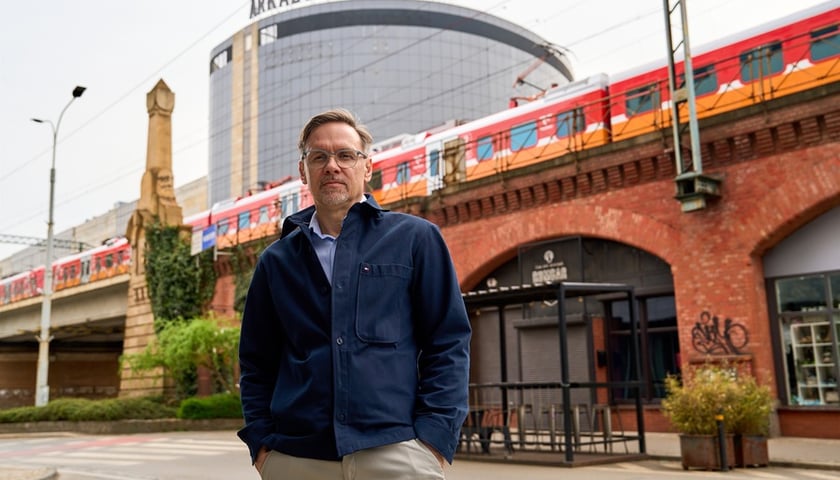 Paweł Szczepaniak na tle nasypu, przejeżdżającego pociągu i Arkad Wrocławskich (kwiecień 2025)