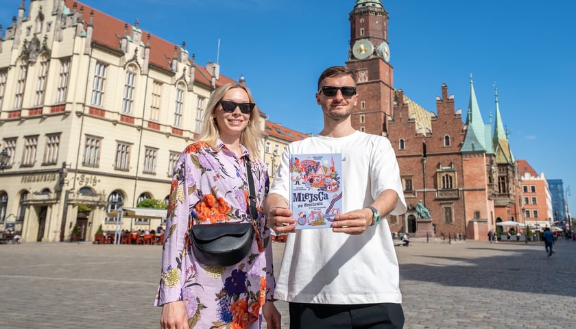 Celina i Kamil Karpińscy, autorzy przewodnika po Wrocławiu dla dzieci. Stoją na Rynku i trzymają przewodnik.