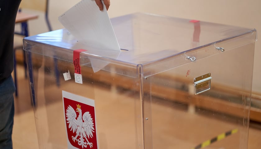 Na zdjęciu urna do głosowania i osoba wrzucająca karty do głosowania. Zdjęcie ilustracyjne